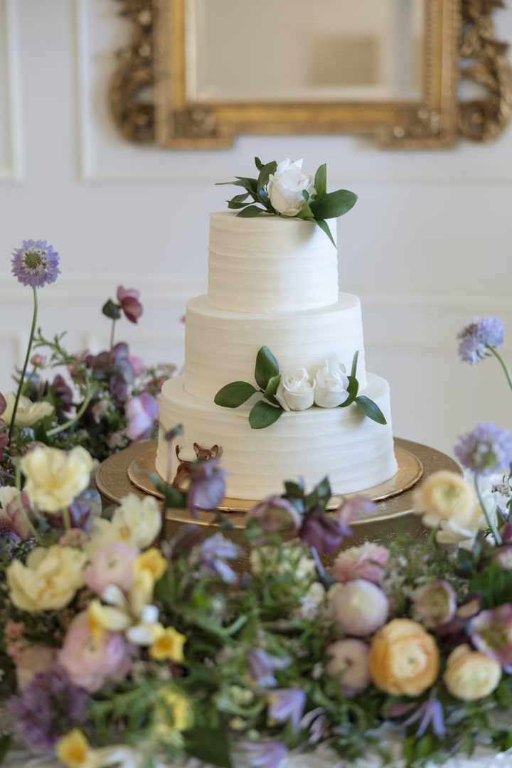 Gorgeous 3-tier white wedding cake surrounded by spring flowers in the ballroom of the Vintage Court southern wedding venue in Covington Louisiana