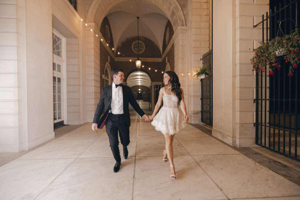 Bride in a short dress walking down the hallway at Hall of Springs in Saratoga NY at night with her groom