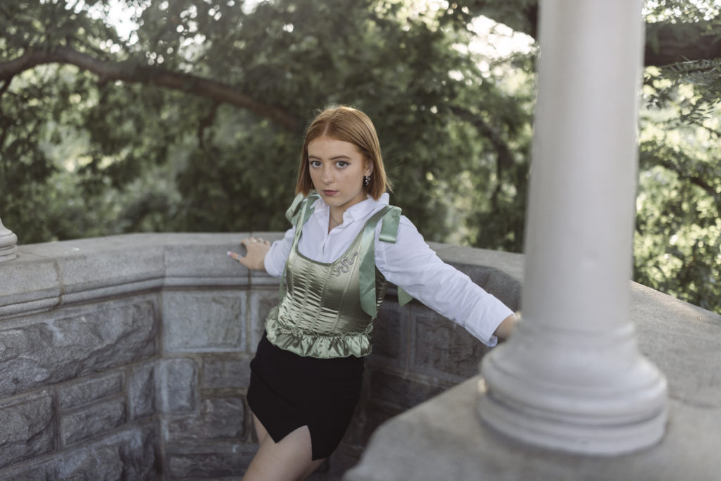 Senior pictures in Central Park in NYC at Belvedere castle wearing a corset top with white shirt underneath.