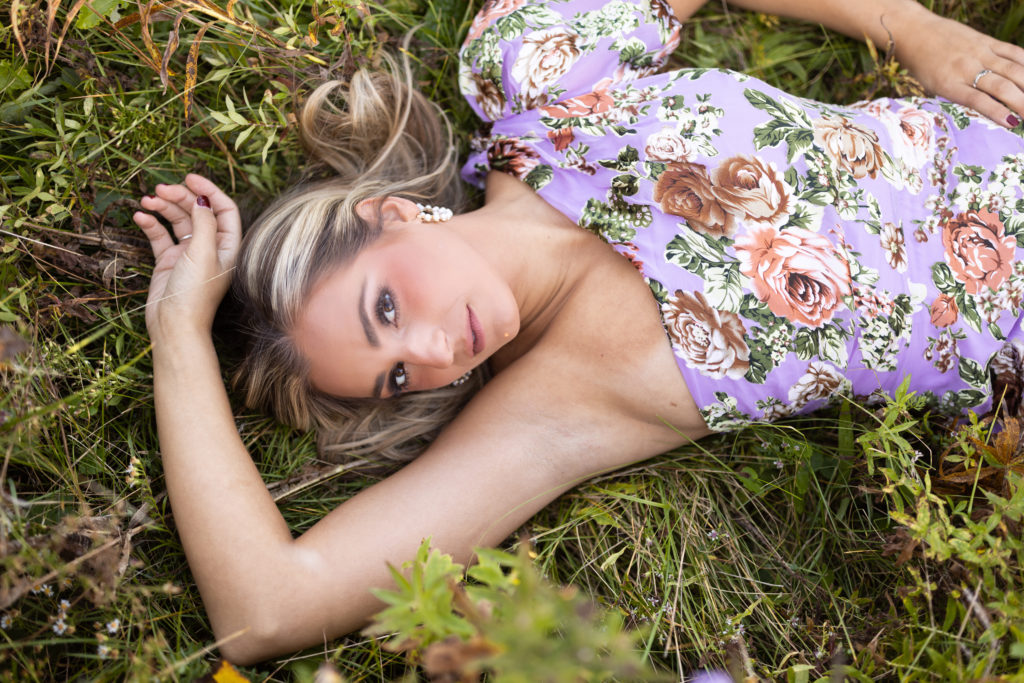 Modeling portraits for Colie lying down in a field while wearing a one-shoulder floral dress