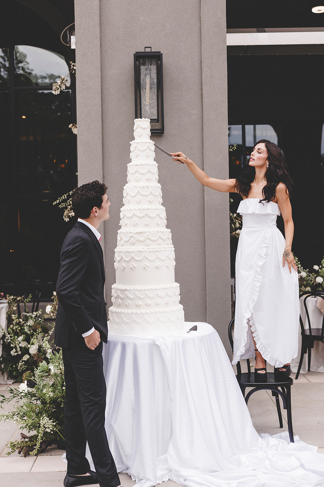 Bride standing on a chair to cut a towering wedding cake at Hotel Vin Rogers.