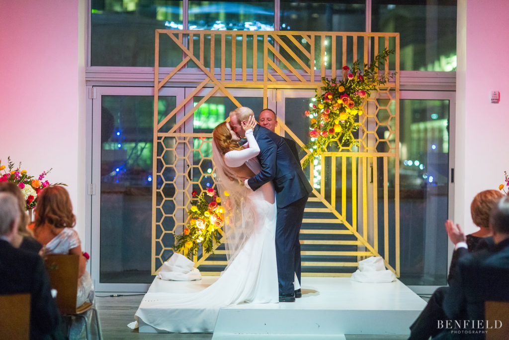 the bride and groom share a first kiss in front of a custom arbor built by the groom for their wedding at the gallery event space in kansas city in the power and light district on new years eve.