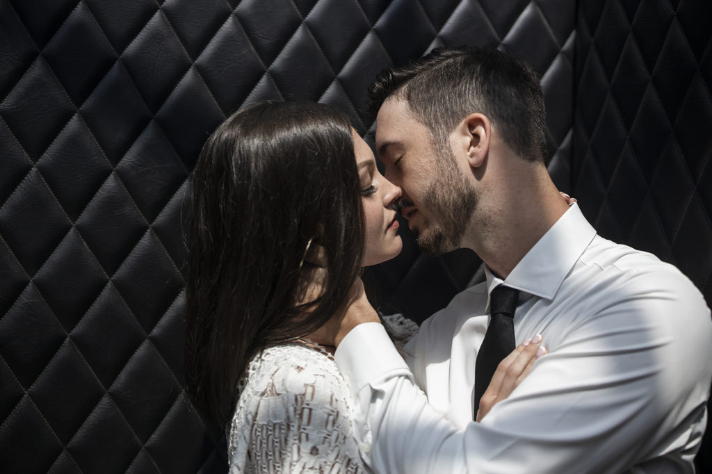 bride and groom kissing in front of black pintuck leather at a bar