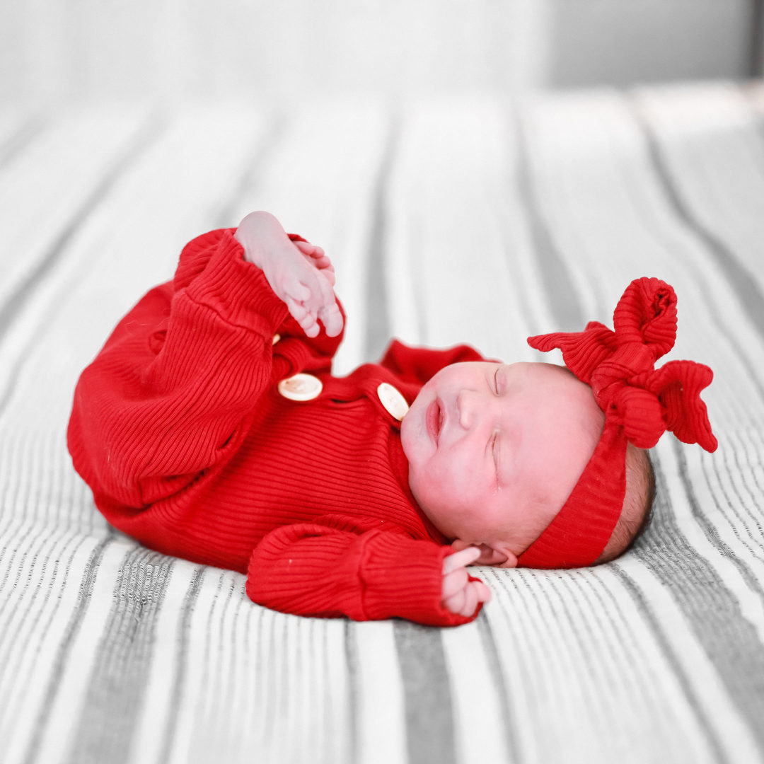 modern family photographer shot of a newborn baby on a bed wearing a cute red outfit