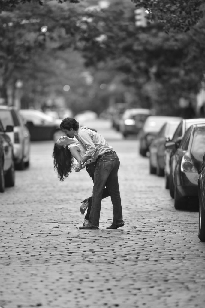 Man dipping woman on the cobblestone streets of new york city for their engagement pictures