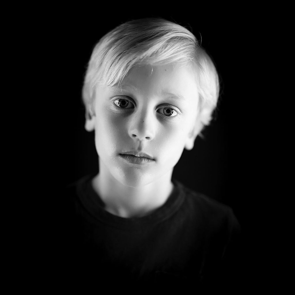 blonde kid photographed in black and white in front of a black background