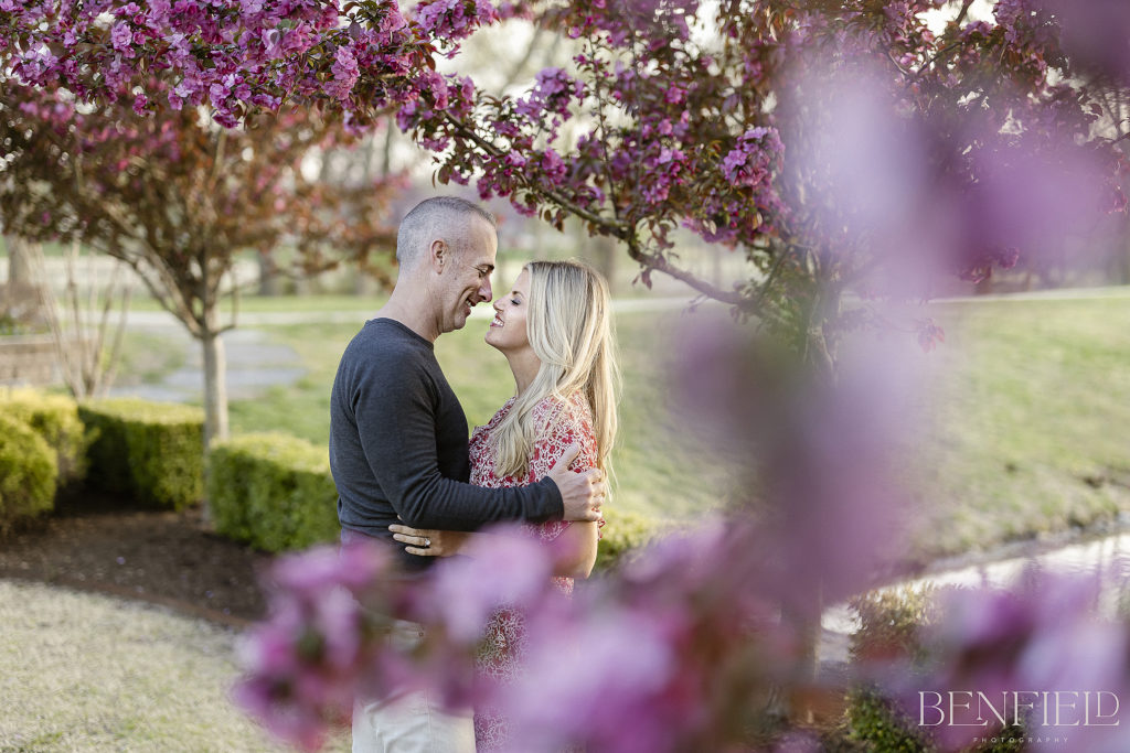 Best Engagement Photos of 2021 nominee is of a bride and groom framed by purple tree blossoms