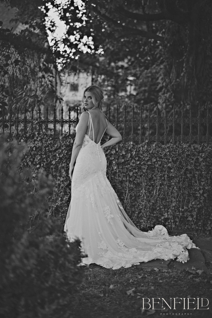 Best Wedding Dresses of 2021 Nominee Jessica wears a stunning backless dress in front of an ivy covered wall with wrought iron fencing.