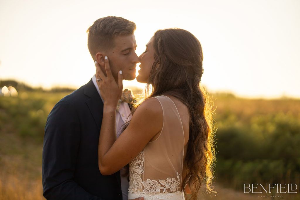 Best Kisses of 2021 Nominee shows a bride and groom kissing in a field at sunset