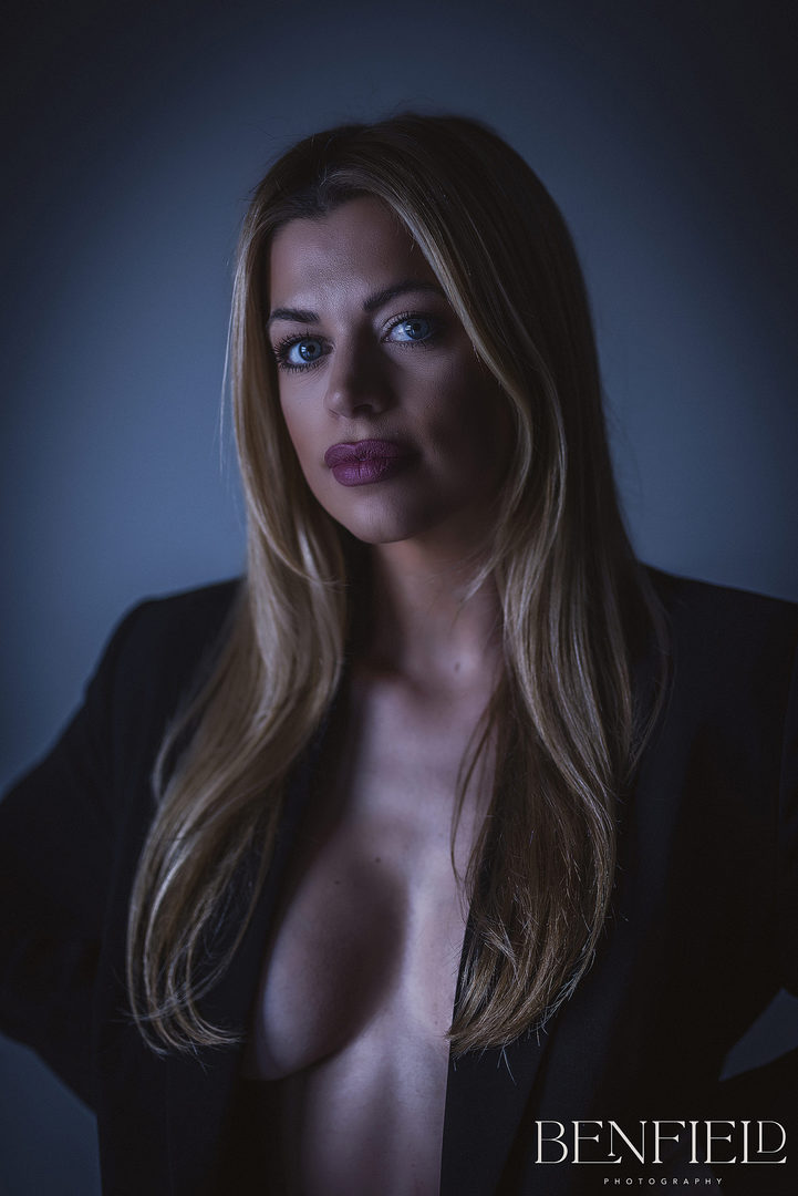 Sexy blonde model wearing no bra and covered with her black suit jacket looking seductively at the camera.