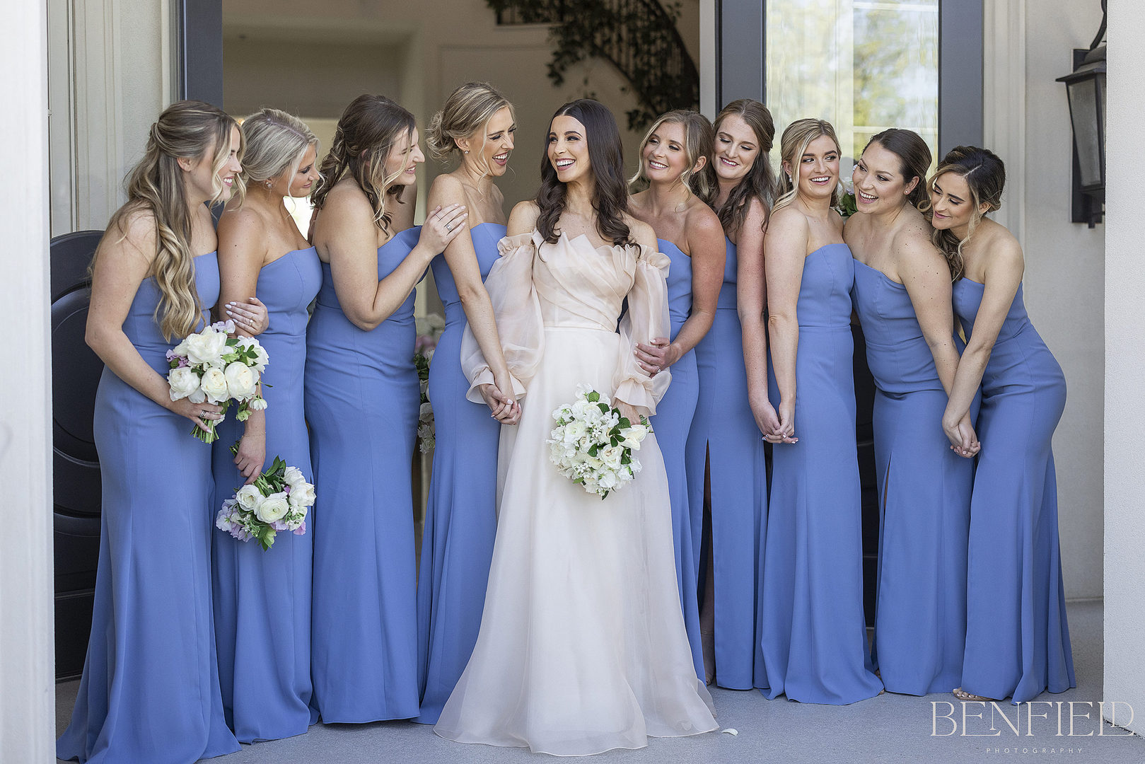 Bride in designer blush wedding gown by Monique Lhuillier standing with her bridesmaids dressed in blue wedding dresses outside of The Hillside Estate