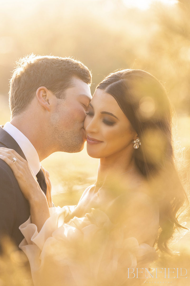 groom kisses his bride on the cheek during sunset golden hour for their wedding portraits at Hillside Estate in Crossroads Texas