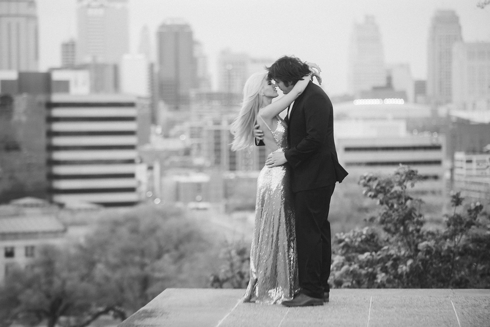 black and white luxury engagement picture of couple with kansas city skyline behind them
