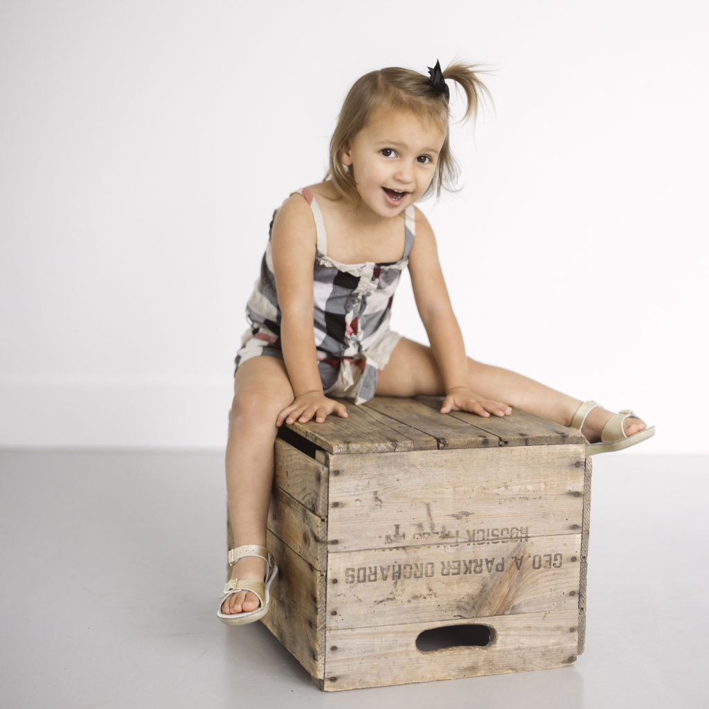 The Best Advice to Photograph Your Own Kids, shown by this toddler girl in burberry romper sitting on a wooden box.