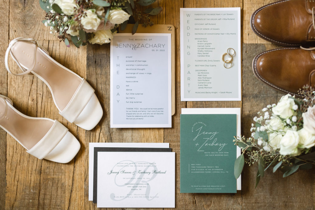 Flat lay of wedding details including wedding invitation, brides shoes, grooms shoes, and florals.