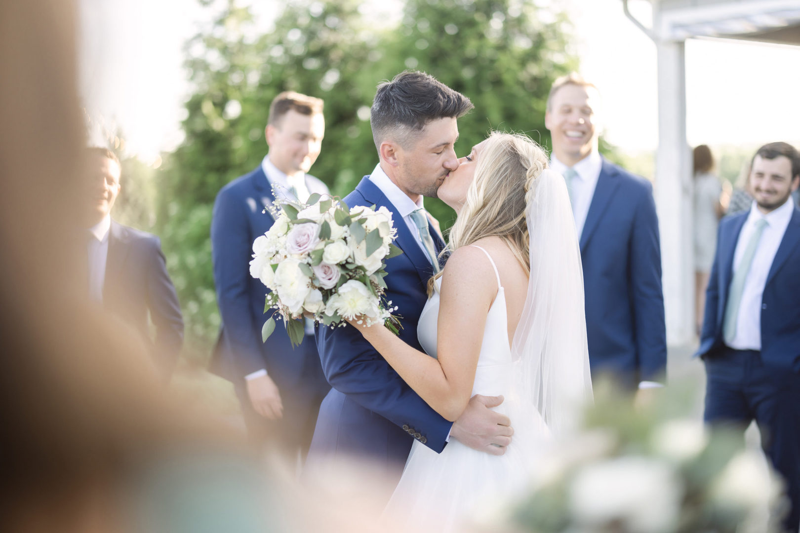 bride and groom kiss amongst their wedding party after being announced husband and wife at Allenbrook Farms luxury wedding venue