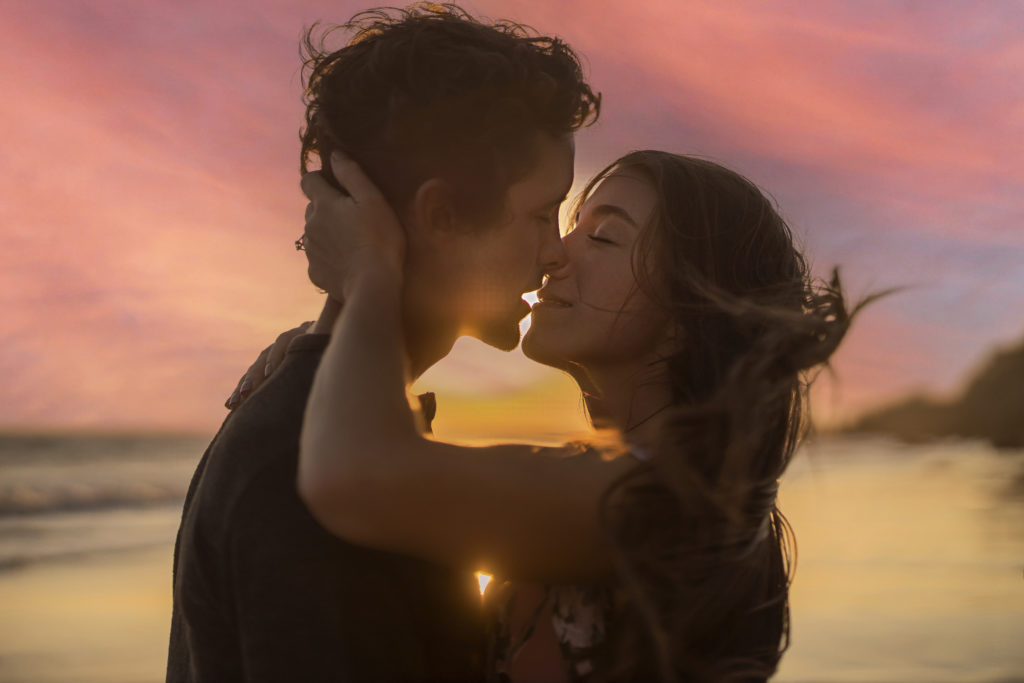 Engagement Portraits in Malibu at sunset with couple kissing and wind blowing her hair