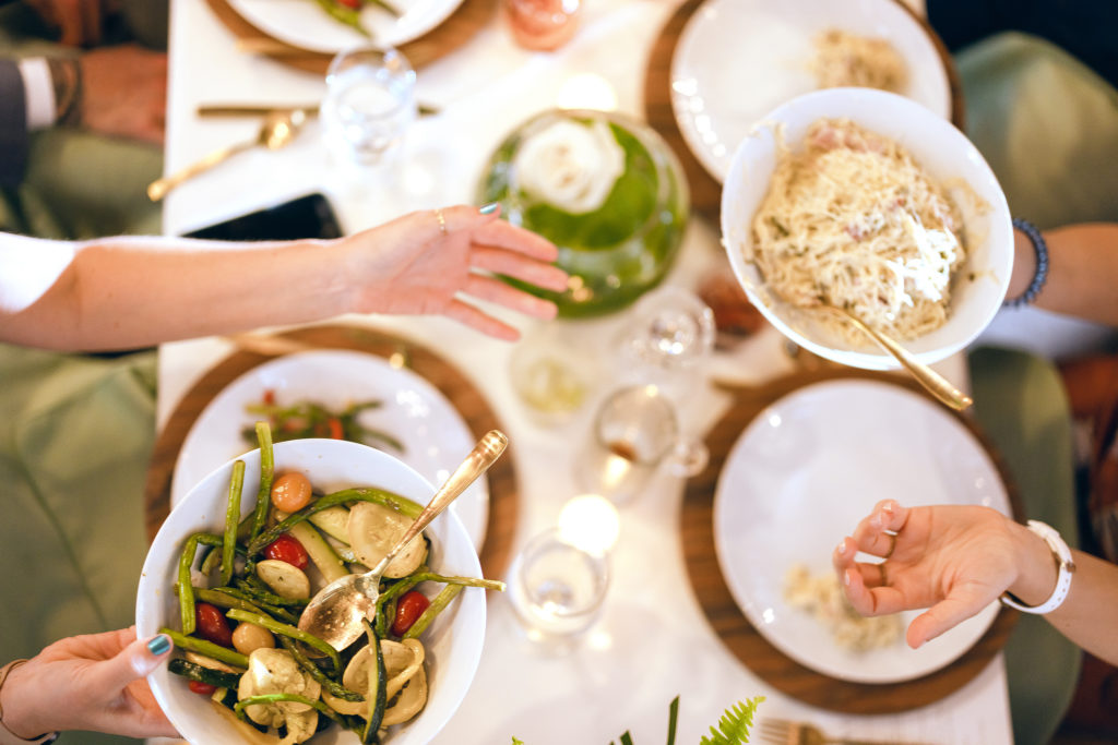 Family Style Dining at Wedding Reception showing guests passing plates of pasta and vegetables across the table.