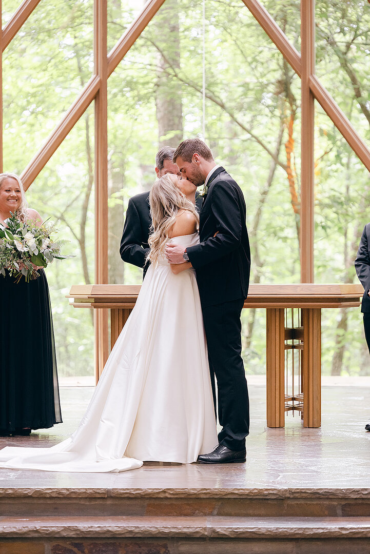 groom kisses bride at glass anthony chapel in garvan gardens