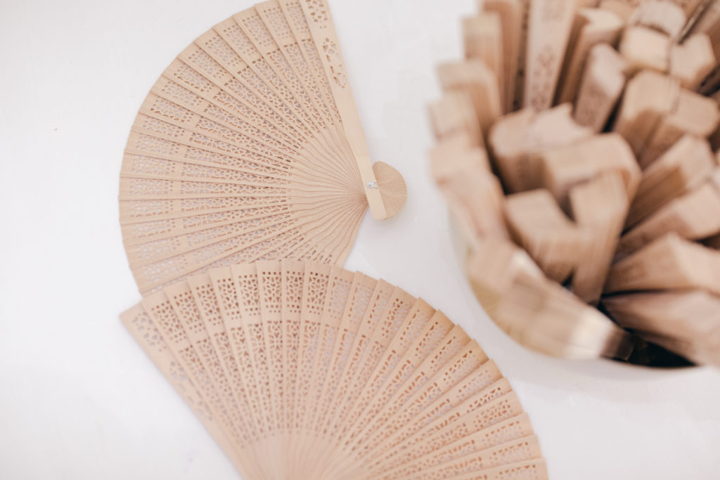 ornate wooden hand fans for guests to use at an outdoor wedding in the summer
