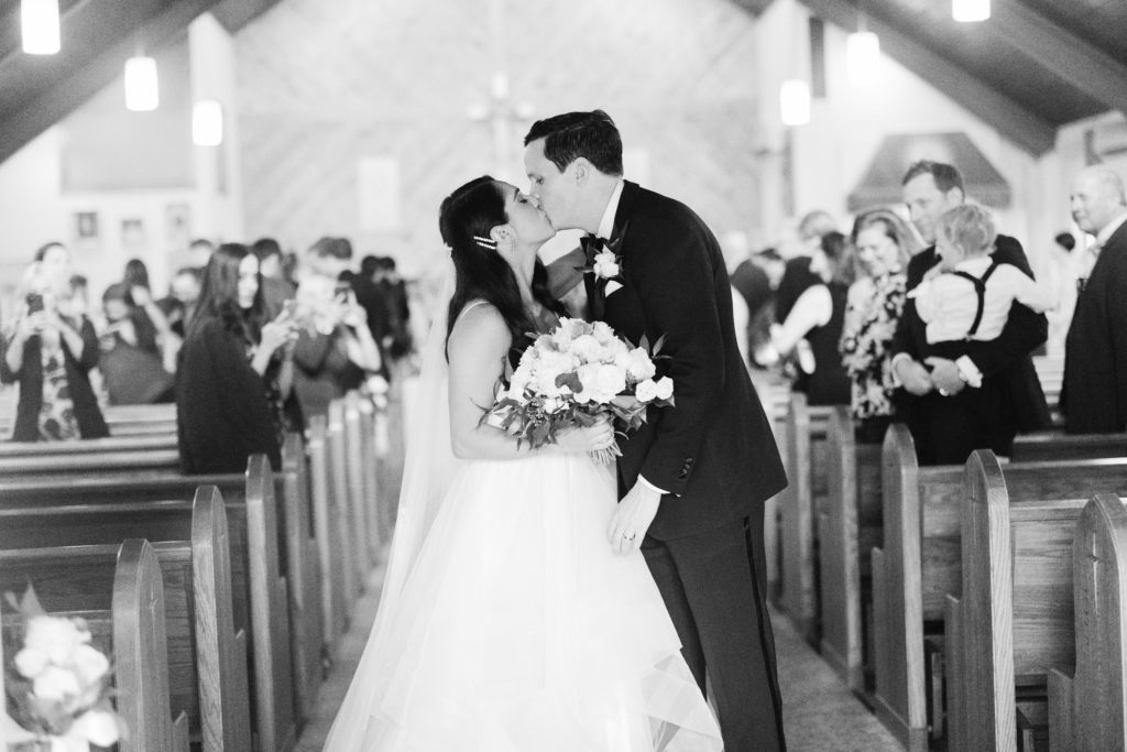 bride and groom kiss at the back of the aisle in the church by the Sagamore wedding on Lake George