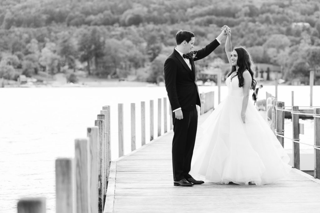 Groom twirls his bride on the wooden dock at The Sagamore for their wedding portraits. This classic black and white image shows the bride and groom in love on their wedding day.