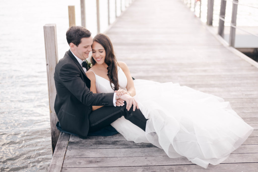 The bride and groom sit on the wooden dock at The Sagamore and snuggle.