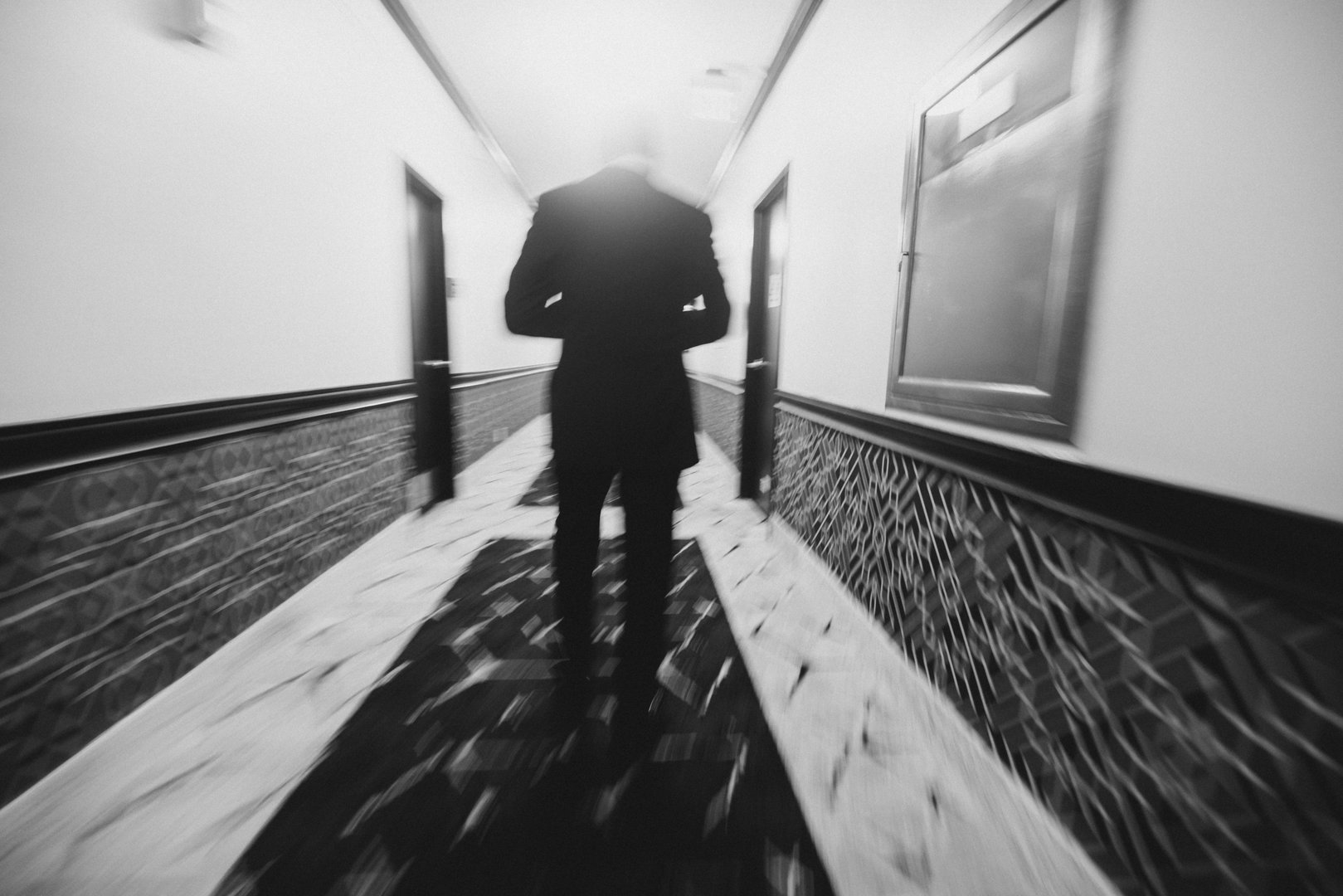 groom from behind walking down the hotel hallway in a blurry black and white image