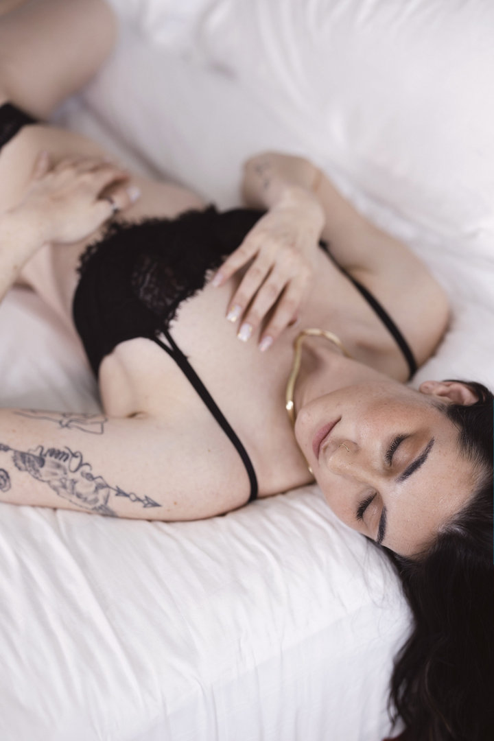 Upscale boudoir portraits of a sexy black haired young woman in black lingerie laying on a bed seductively.