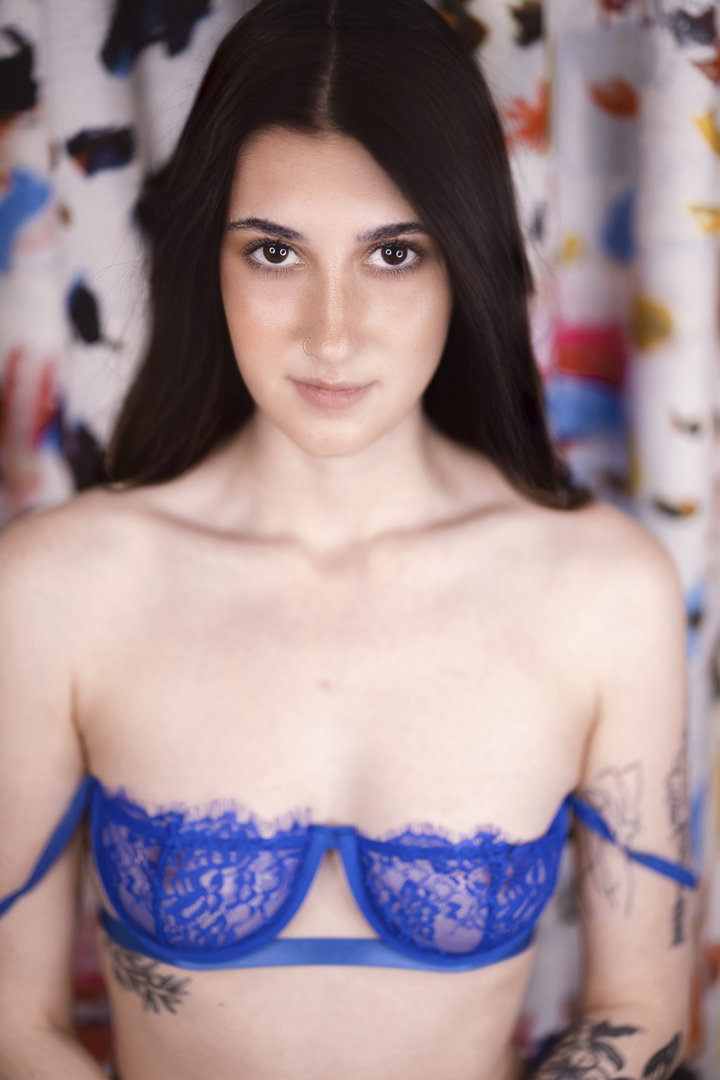 upscale boudoir portrait of a young black haired female in a blue lace panty and bra on a floral couch.