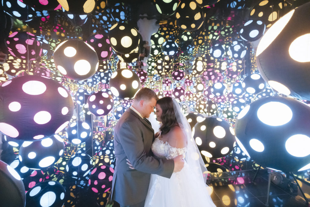 The bride and groom pose in the infinity room for a luxury Crystal Bridges wedding surrounded by neon balls