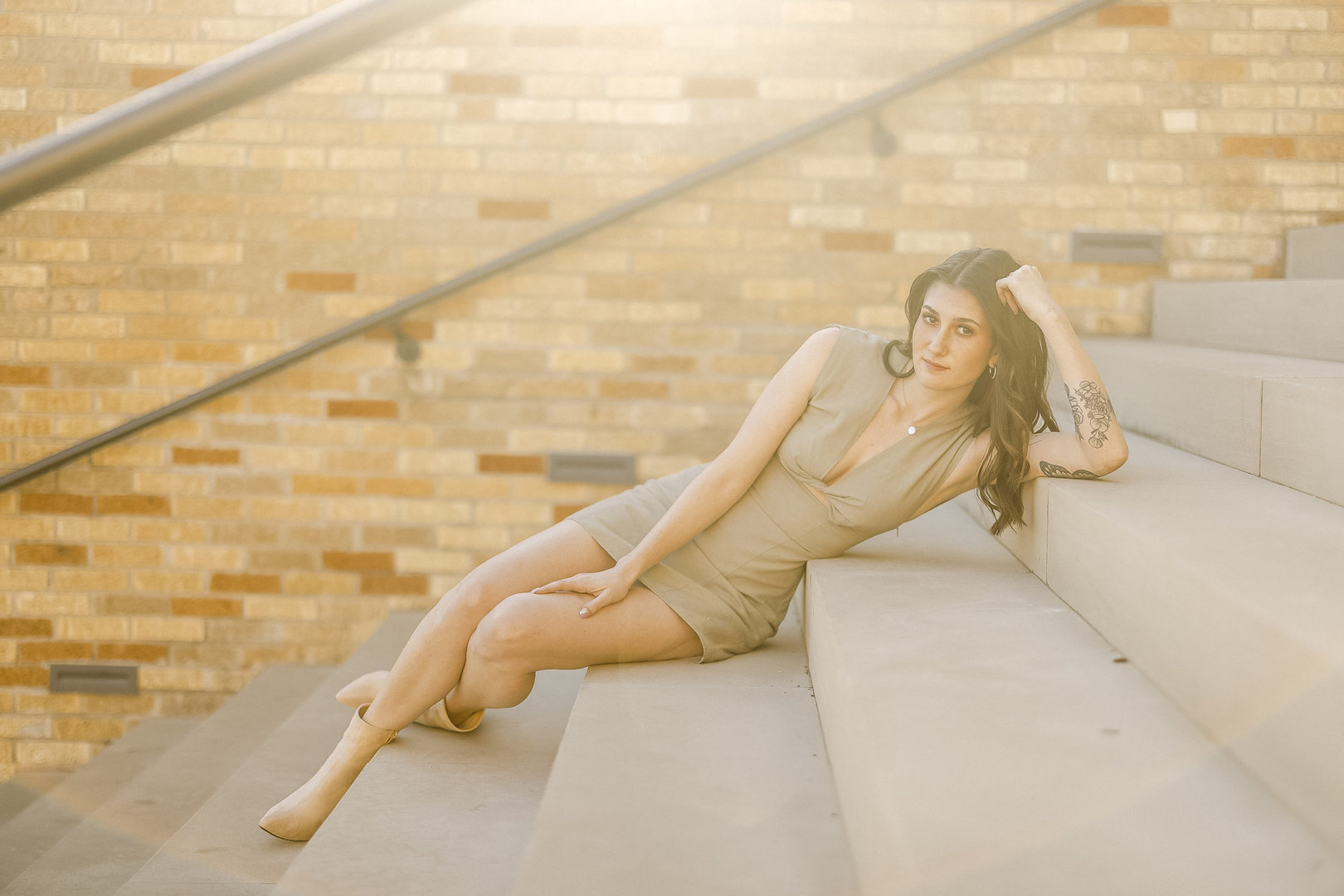 Sexy model with dark hair dresses in a short dress lying down on stair for a NW Arkansas model photographer.
