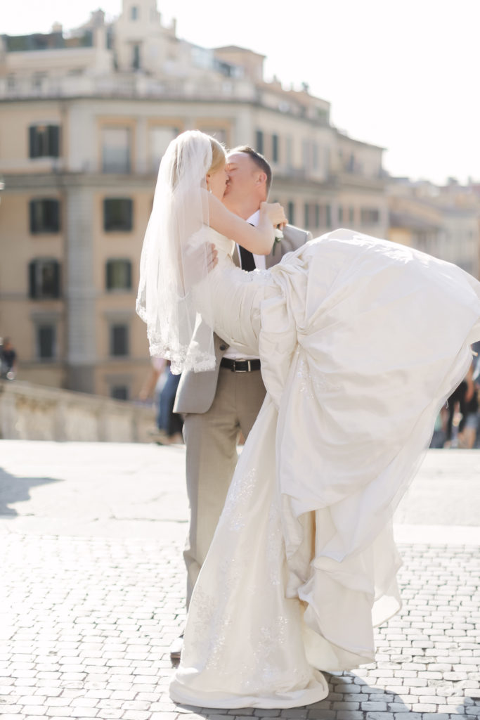 US American wedding photographer in Rome, Italy, photographing a groom holding up his bride and kissing her in the public square in Rome. 