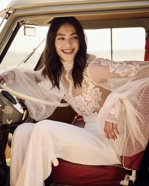 Costarellos Luxury Bridal dress that is a white blouse and pants the bride is wearing while sitting in an antique car with the door open.