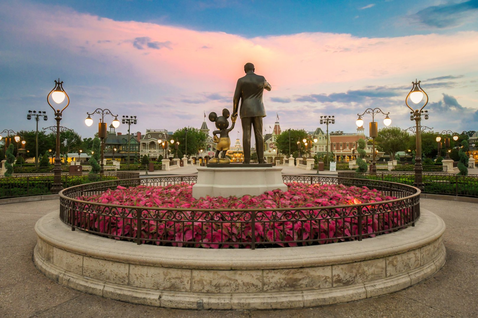 Disney Vacation Tips to make it seem like you're the only one at Disneyworld with no wait times on rides, like you see here in this picture of Walt Disney holding Mickey Mouse's hand at sunset.