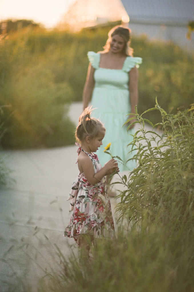 mom + daughter video vignette of little girl playing in a field of yellow flowers with her mother looking on