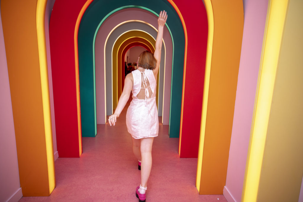 Senior Pictures at Museum of Ice Cream of teenage girl with red hair in a rainbow archway