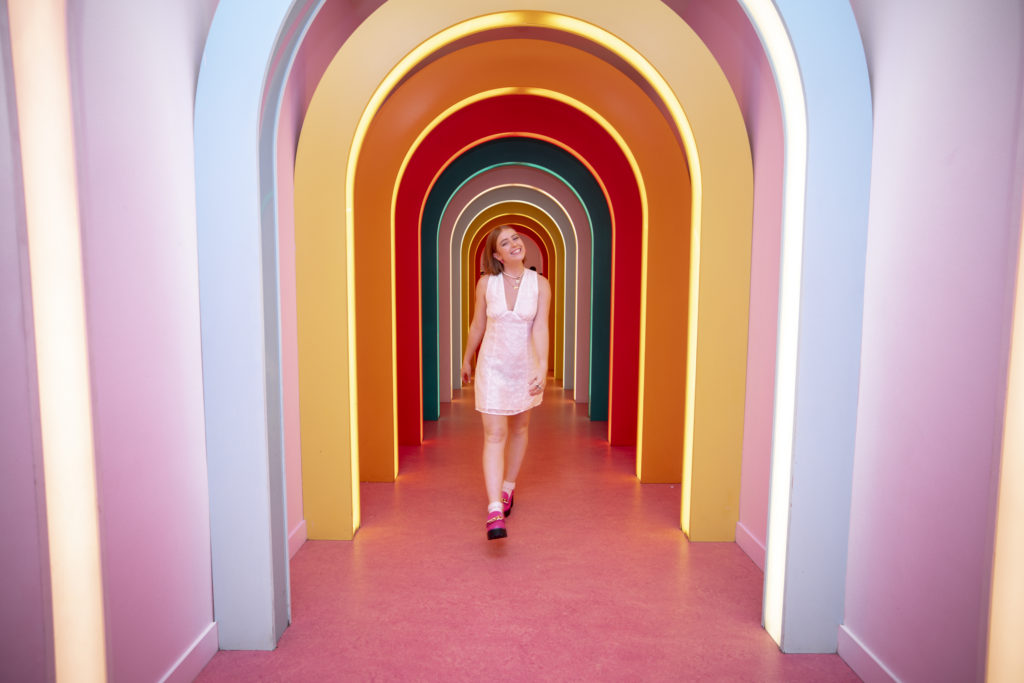 Senior Pictures at Museum of Ice Cream of teenage girl with red hair in a rainbow archway