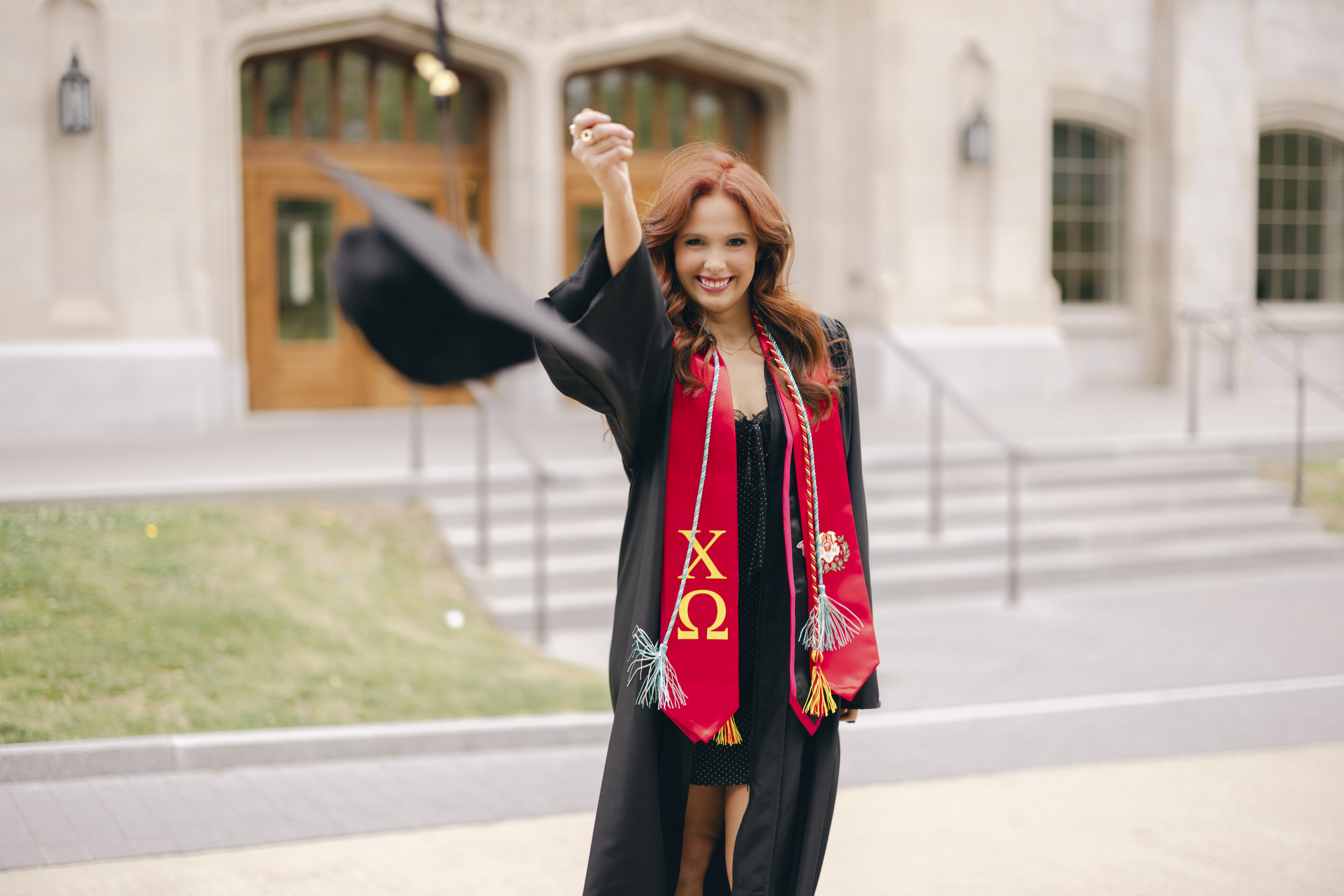 Graduate Portraits at University of Arkansas of gorgeous redhead college senior throwing her cap and wearing her gown.