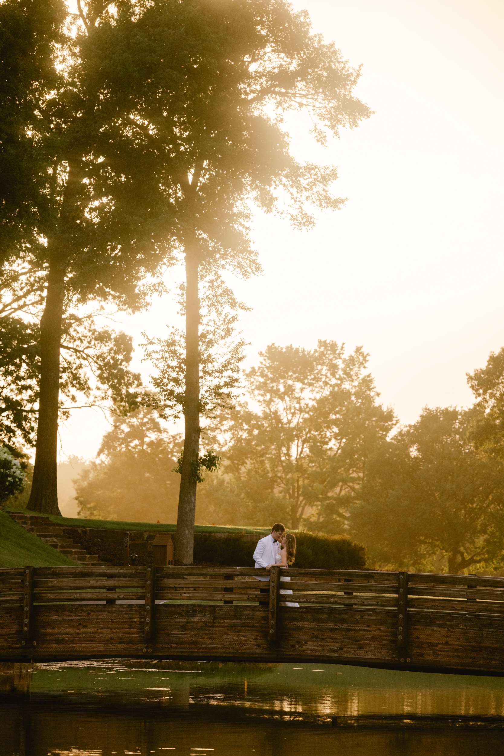 Pinnacle Country Club Wedding Portrait of a bride and groom at sunset with tall trees and standing on a wooden bridge.
